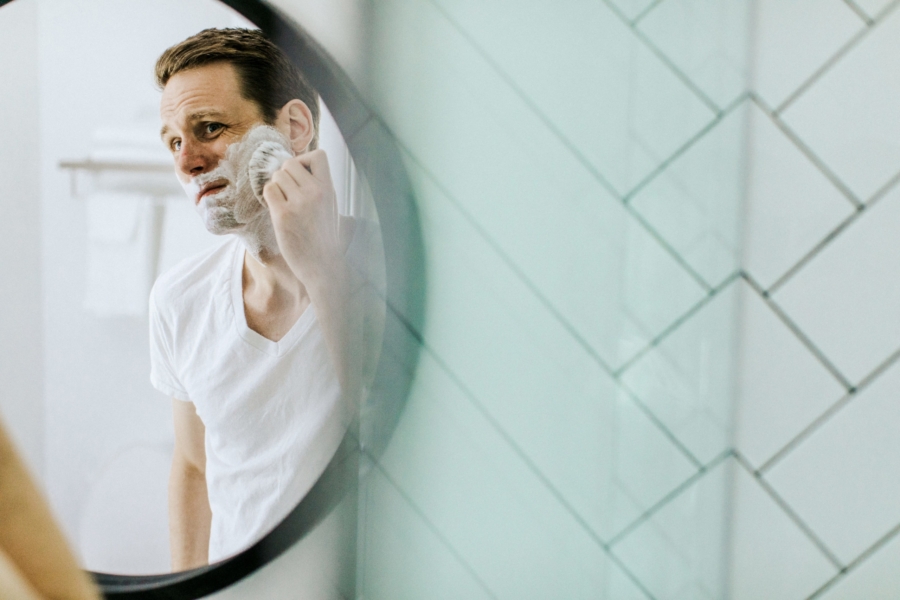 Man looking in the mirror applying shaving cream containing sodium lauryl sulfate.