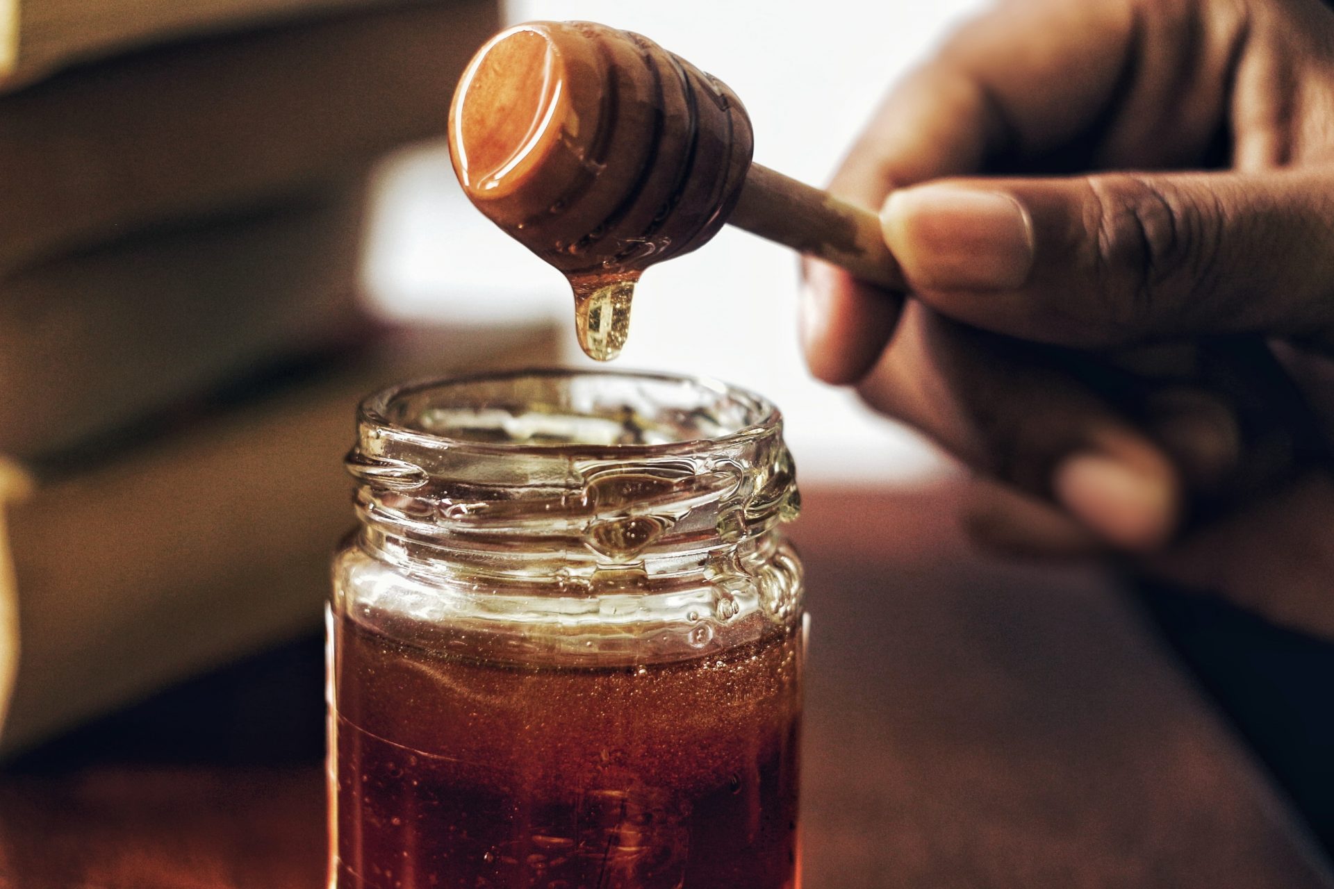 Man dipping honey from a glass jar.