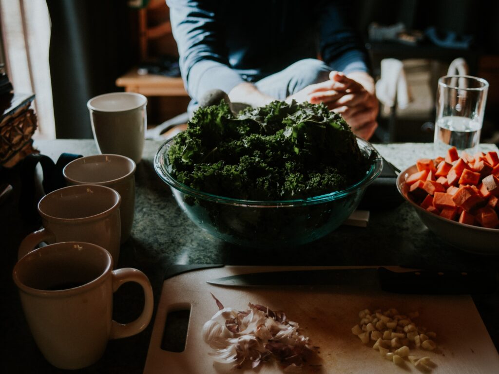 Woman sitting at a table with bowls of cruciferous veggies.