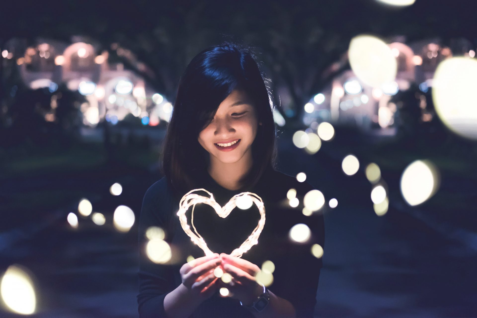 Woman smiling as she looks at a heart-shaped string of lights that she's holding.