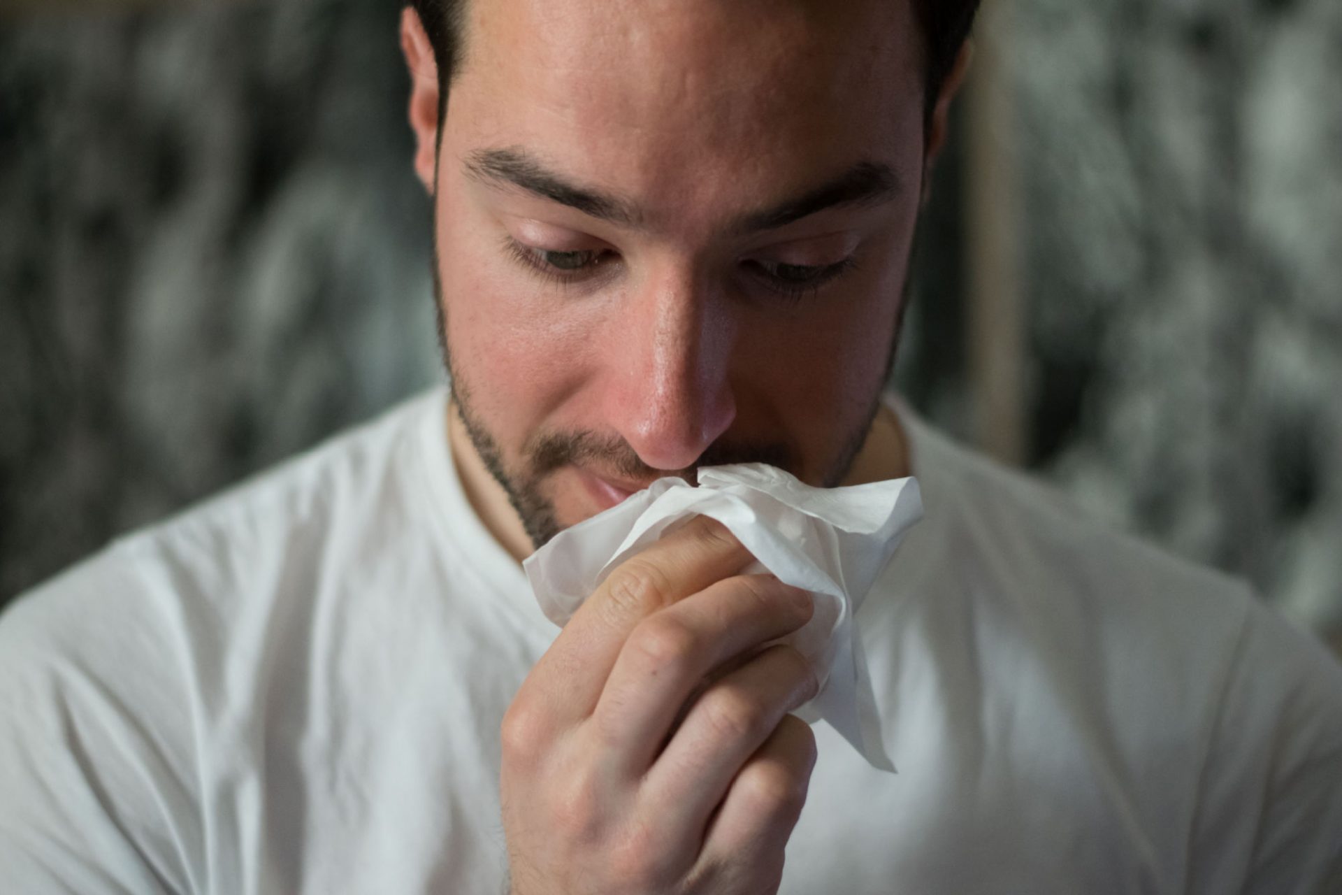 Man wiping his nose with a tissue.