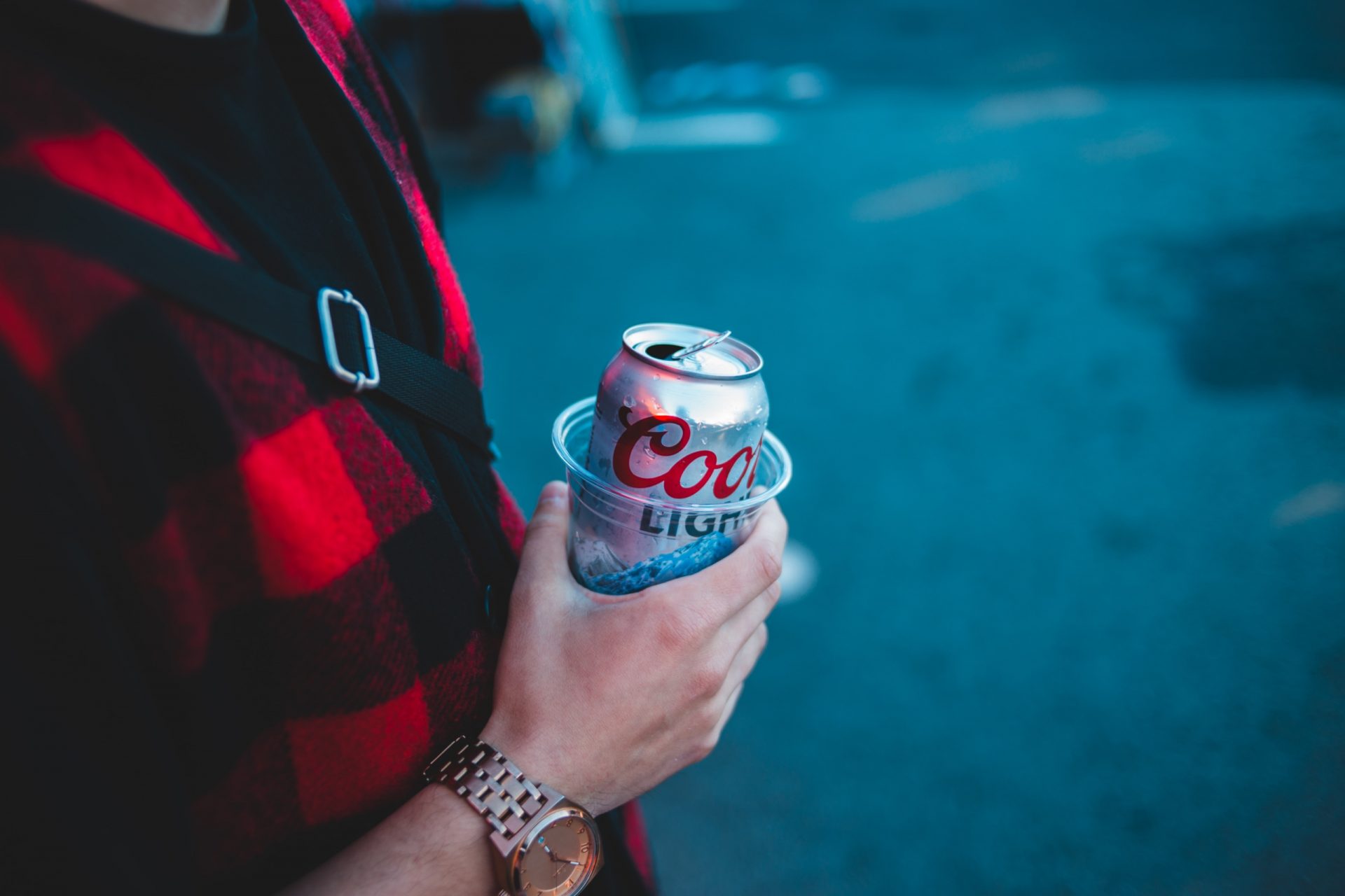 Man holding an aluminum can of beer in a plastic cup.