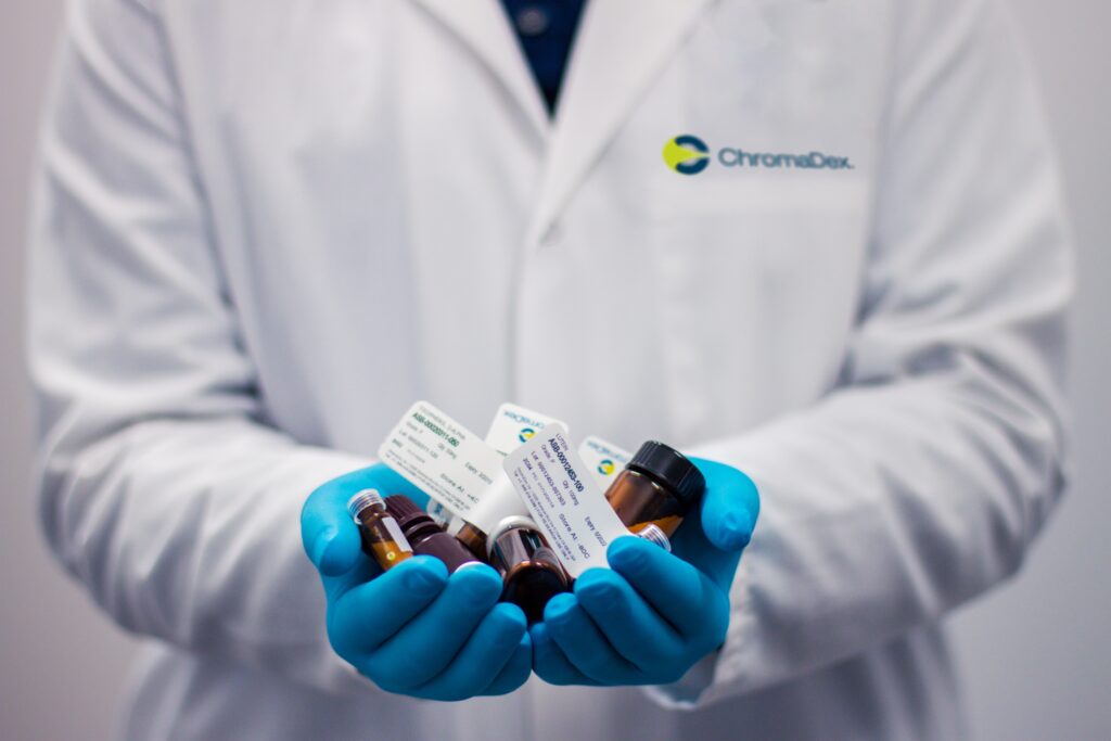 Man wearing a white lab coat and latex gloves holding prescription bottles.