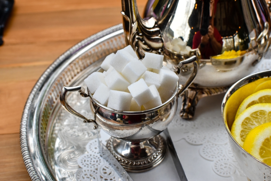 Sugar cubes in a silver bowl next to a tea pot and lemons