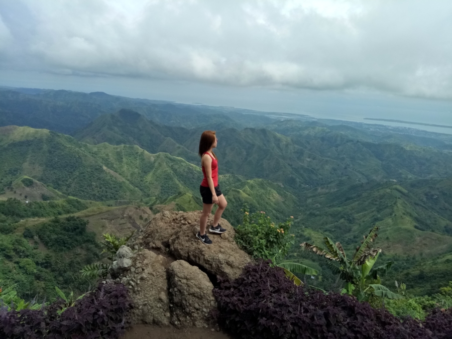 Woman standing on a rock outcropping overlooking a lush valley.