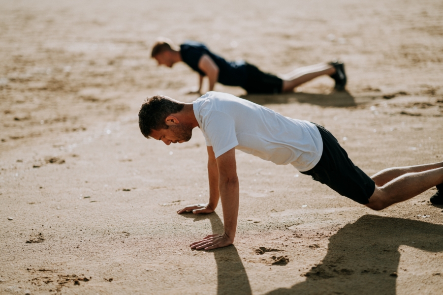 Two men doing pushups on sand in their quest for optimal health and performance.