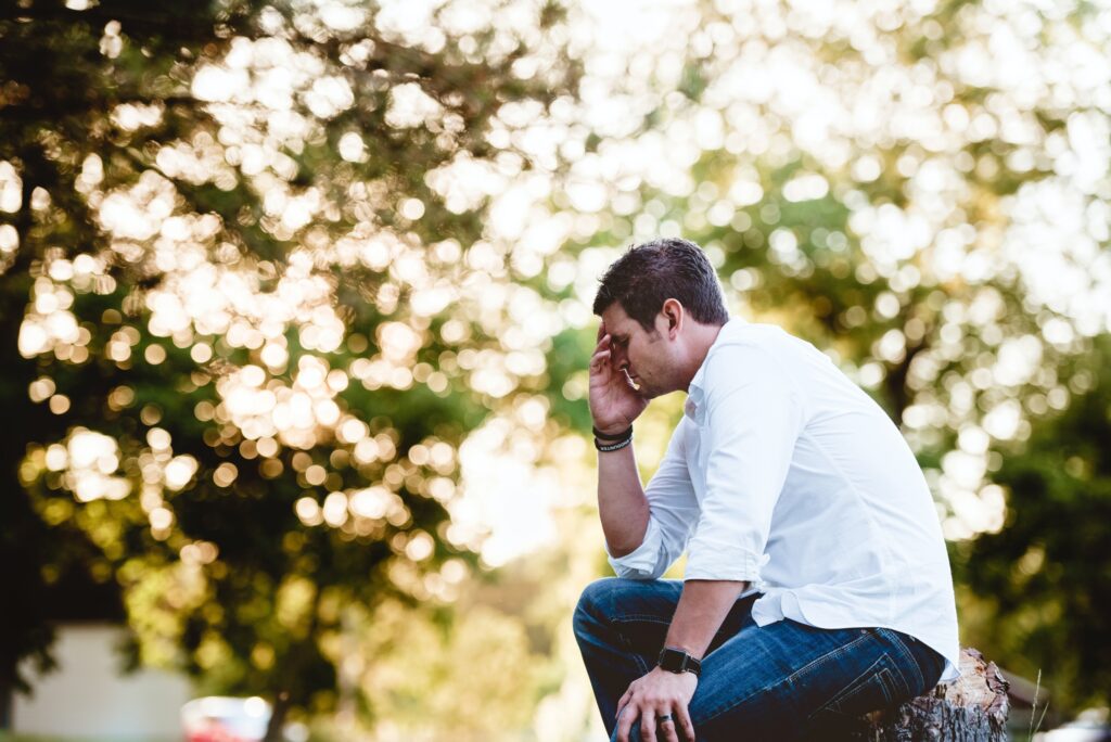Man sitting on a stump with his head in his hand wondering how to overcome anxiety.