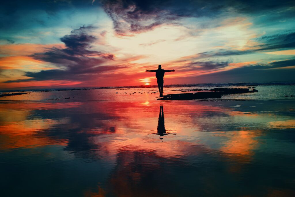 Man standing on the shore with his arms outstretched as he watches the sunrise.