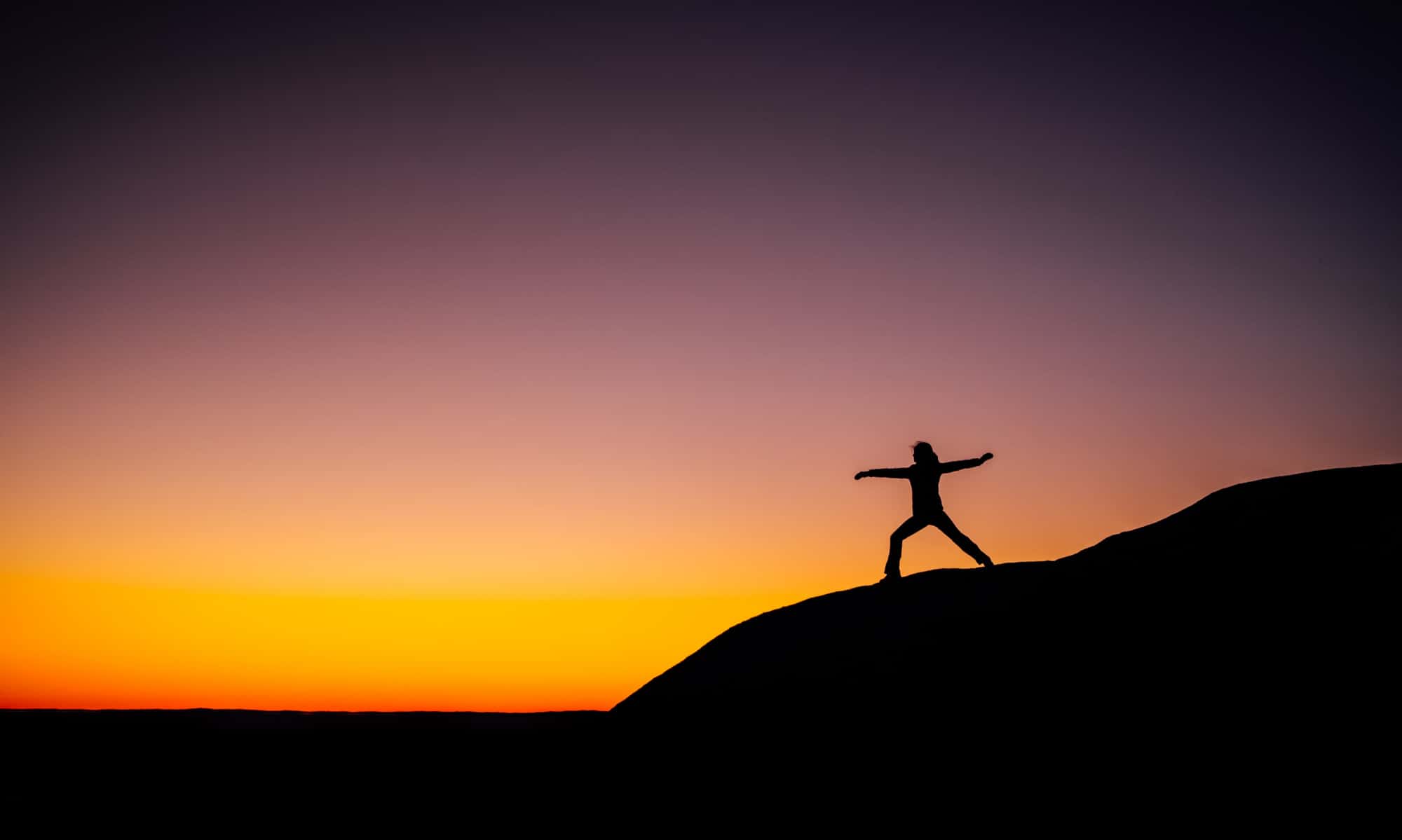 Woman doing yoga on a hill at sunset.