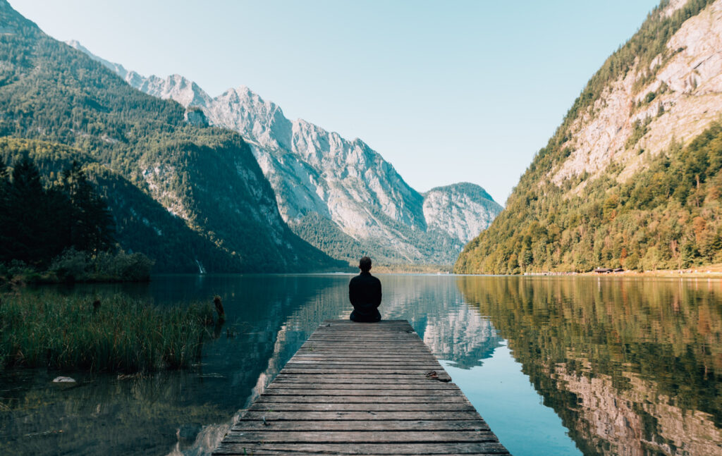 Man sitting on a pier in a mountain lake enjoying his stress-free healthy life.