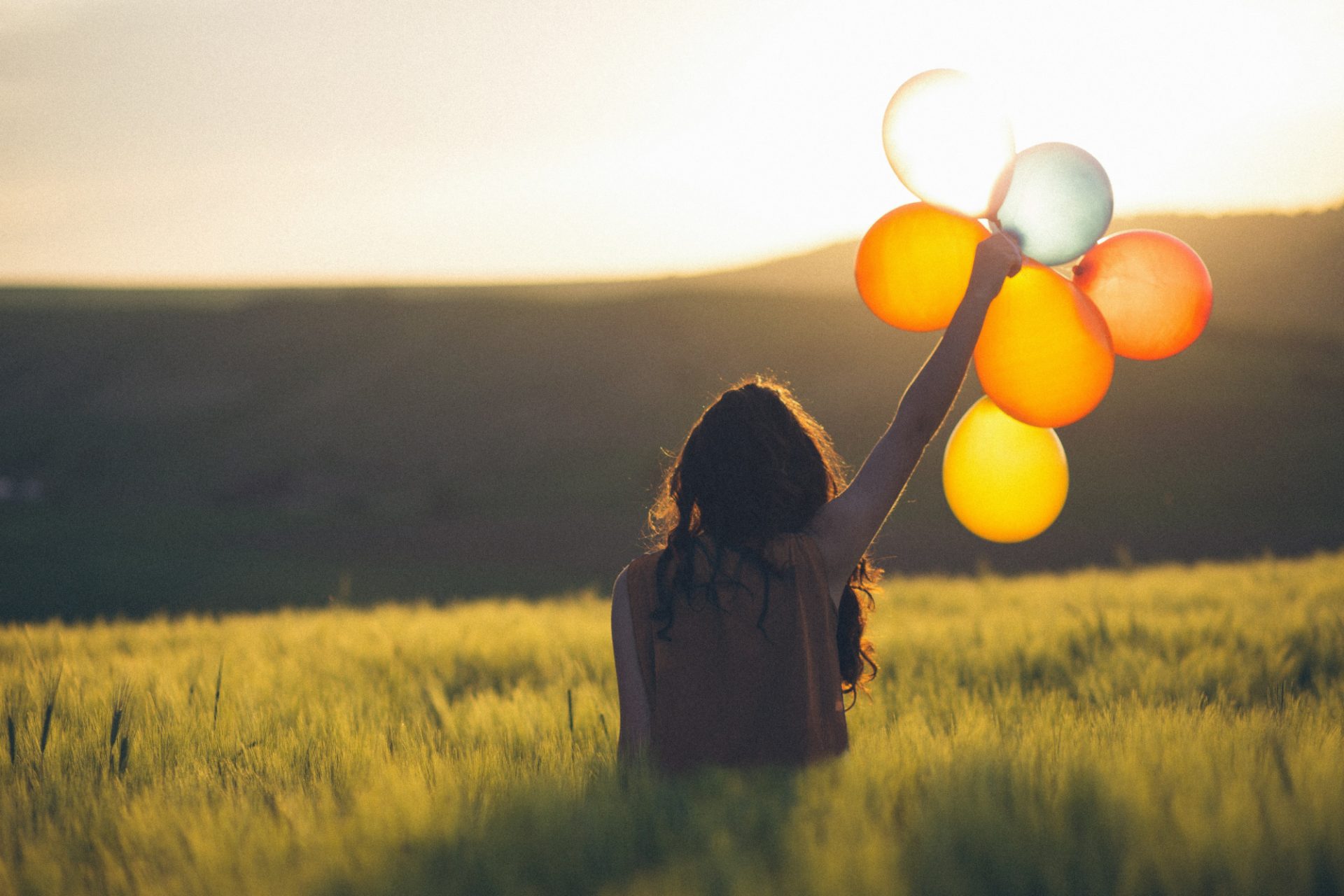 Woman standing in a field holding yellow balloons.