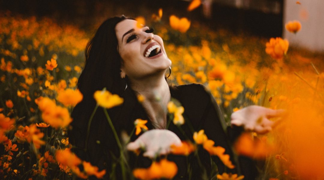 Woman sitting in a field of flowers and smiling.