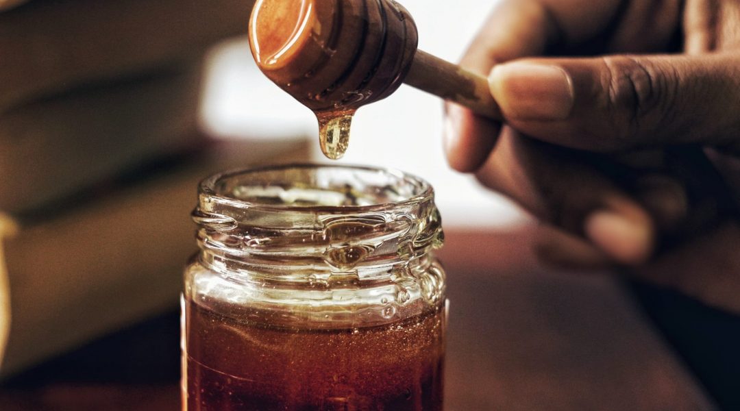 Man dipping honey from a glass jar.