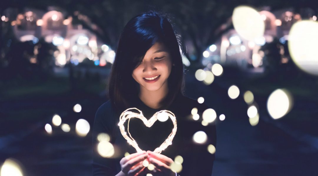 Woman smiling as she looks at a heart-shaped string of lights that she's holding.