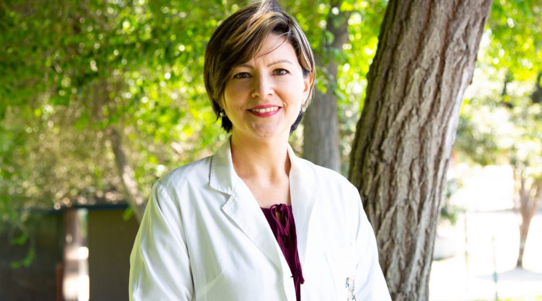 Female doctor wearing a white coat standing outside under a tree.