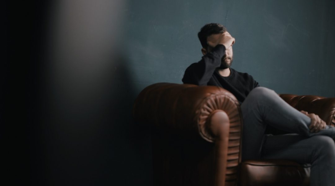 Man sitting in a chair holding his head as he struggles with managing stress and anxiety.