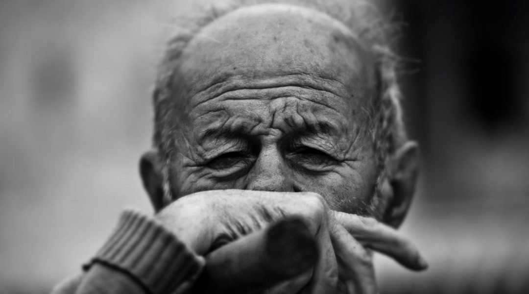 Elderly man with his hand covering his mouth in obvious discomfort.