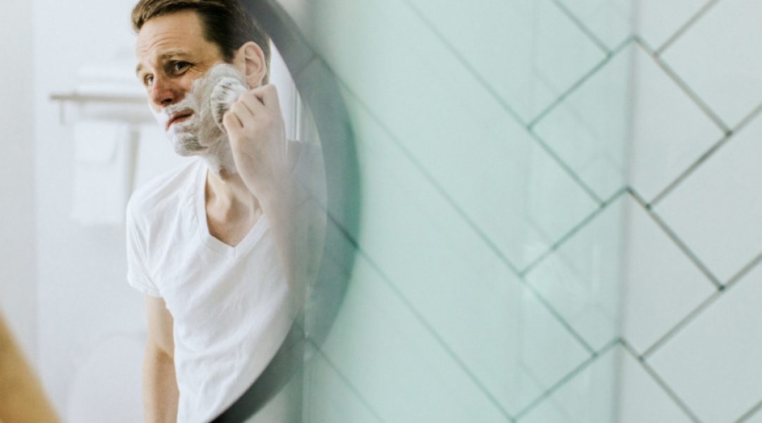 Man looking in the mirror applying shaving cream containing sodium lauryl sulfate.